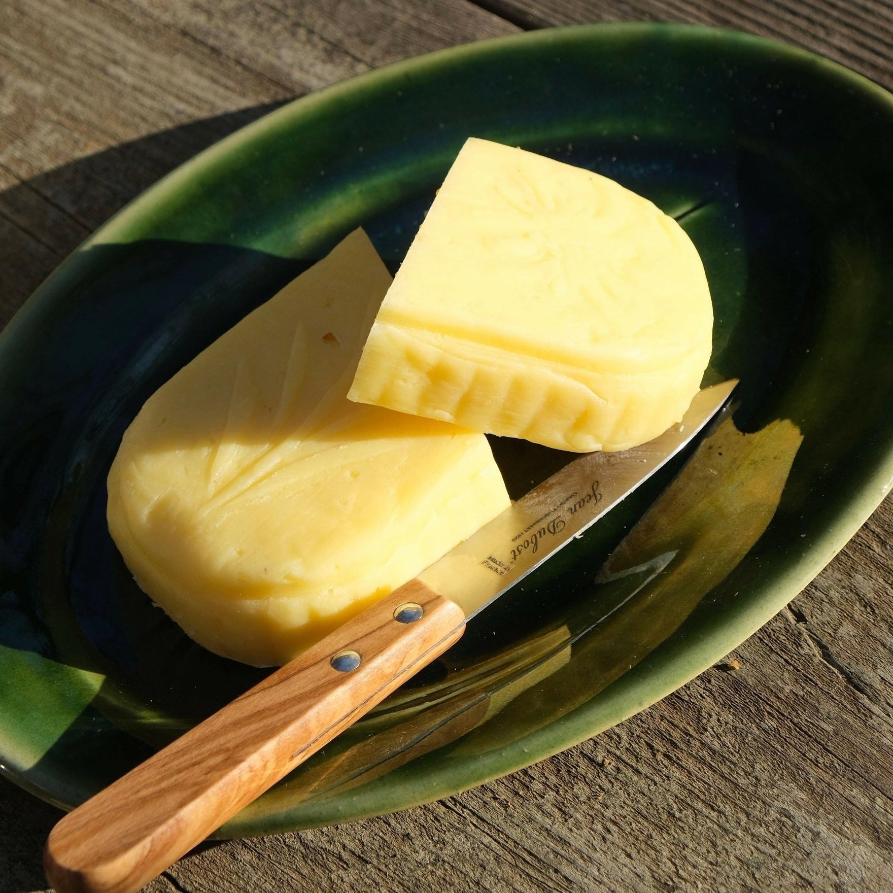 MANTRA LIVING Jean Dubost olive wood paring knife resting on a green ceramic dish with a wedge of butter.