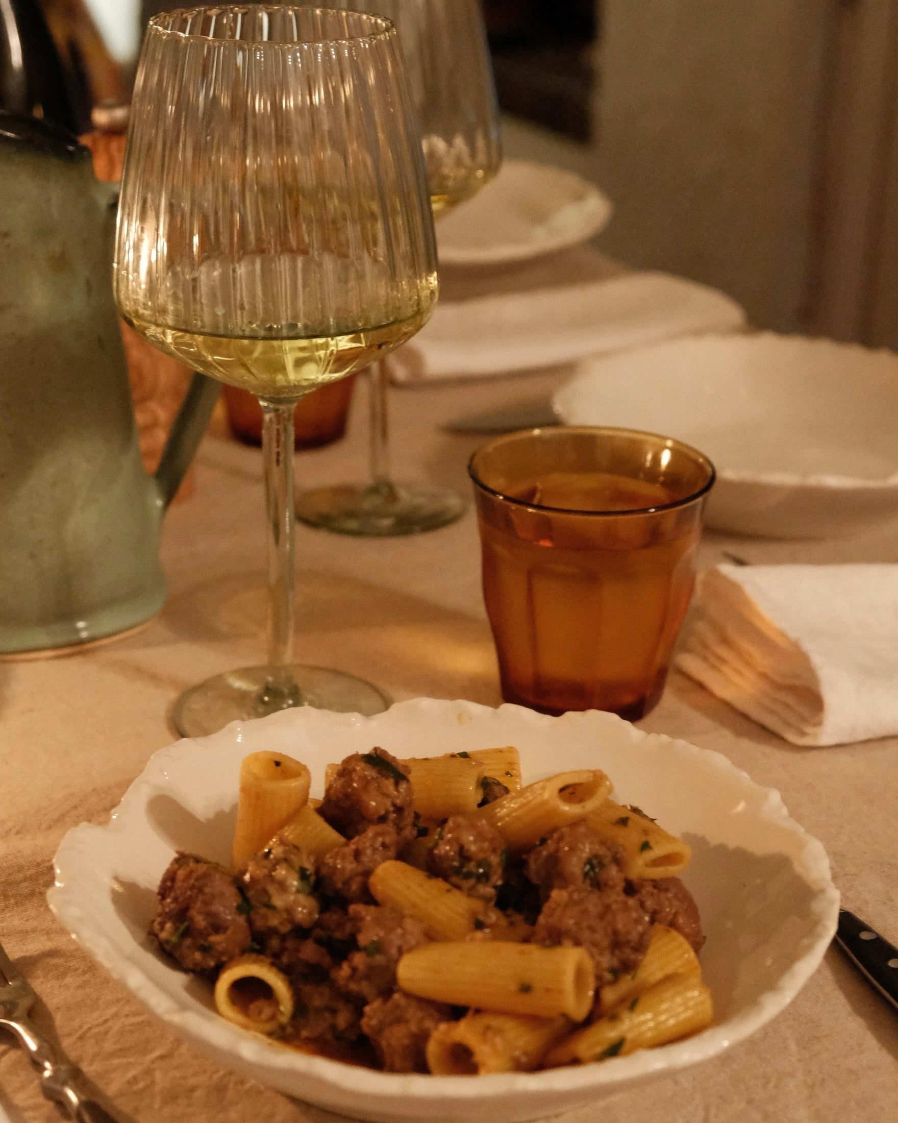Mantra Living Raw-edged Pasta Bowl served with rigatoni, beside a glass of white wine and an amber tumbler.