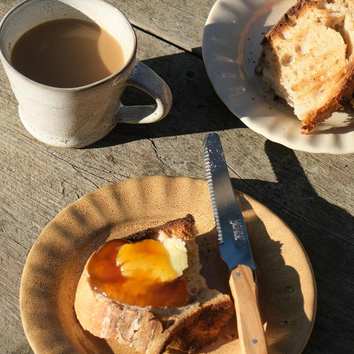 Mantra Living Daisy side plate in Kalahari with toast and honey, beside coffee and a slice of cake in morning light. #Color_Kalahari