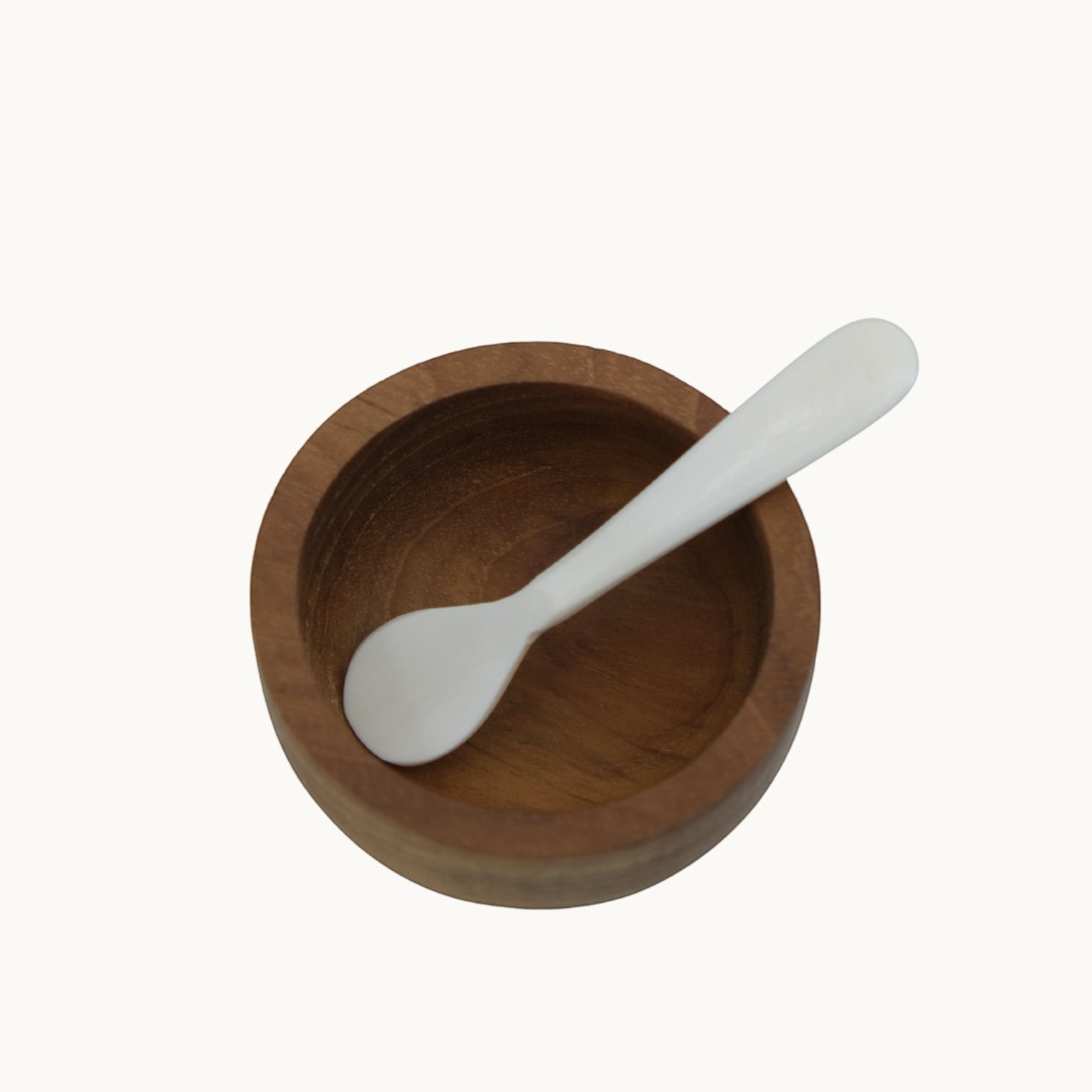 Mantra Living teak salt pinch pot in the small size, seen from above with a white bone salt spoon resting across the bowl. #Size_Small