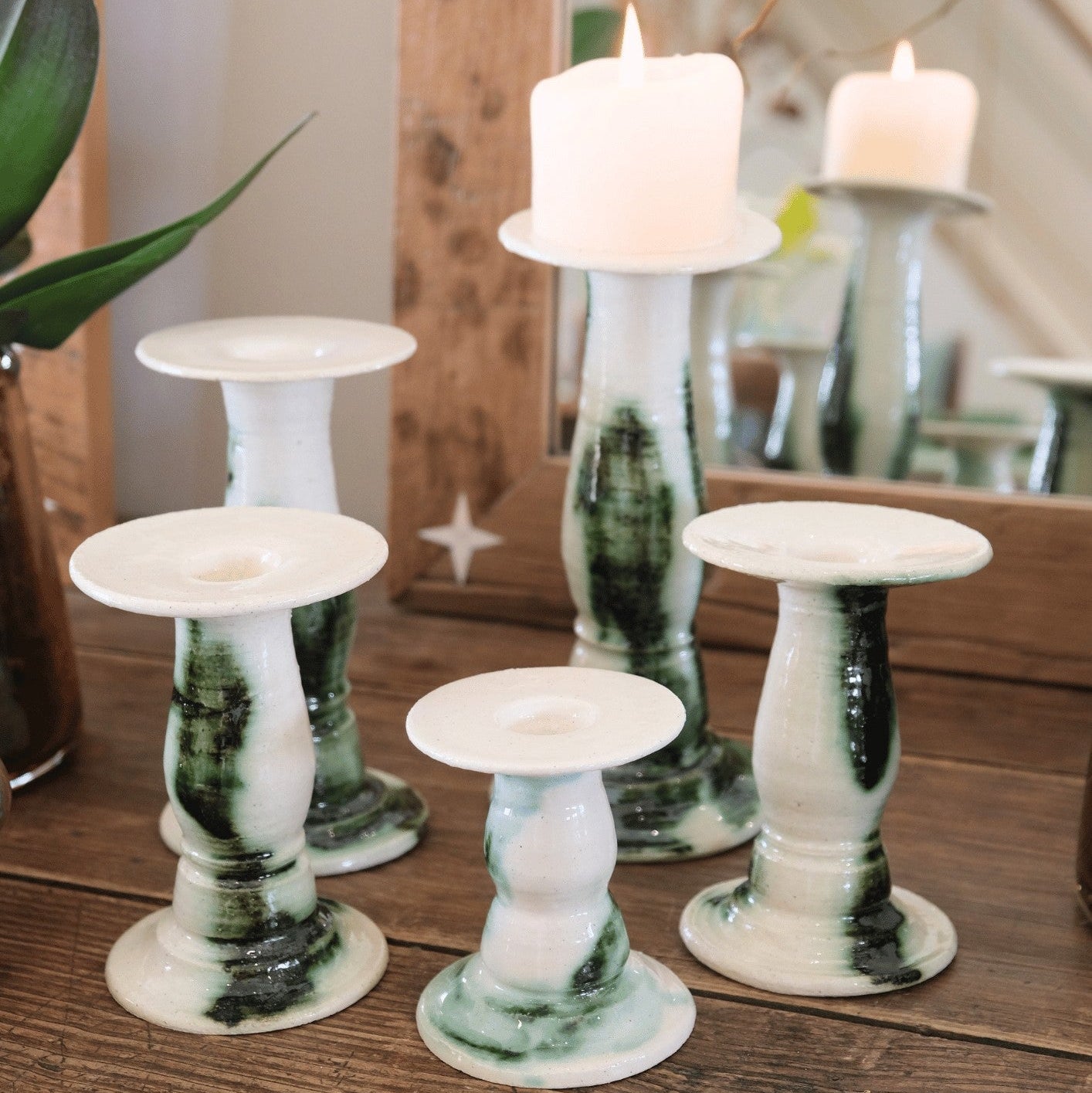 Five Siena candlestick holders in cream and green marbled ceramic grouped on a wooden table with lit pillar candles. #Color_Verde