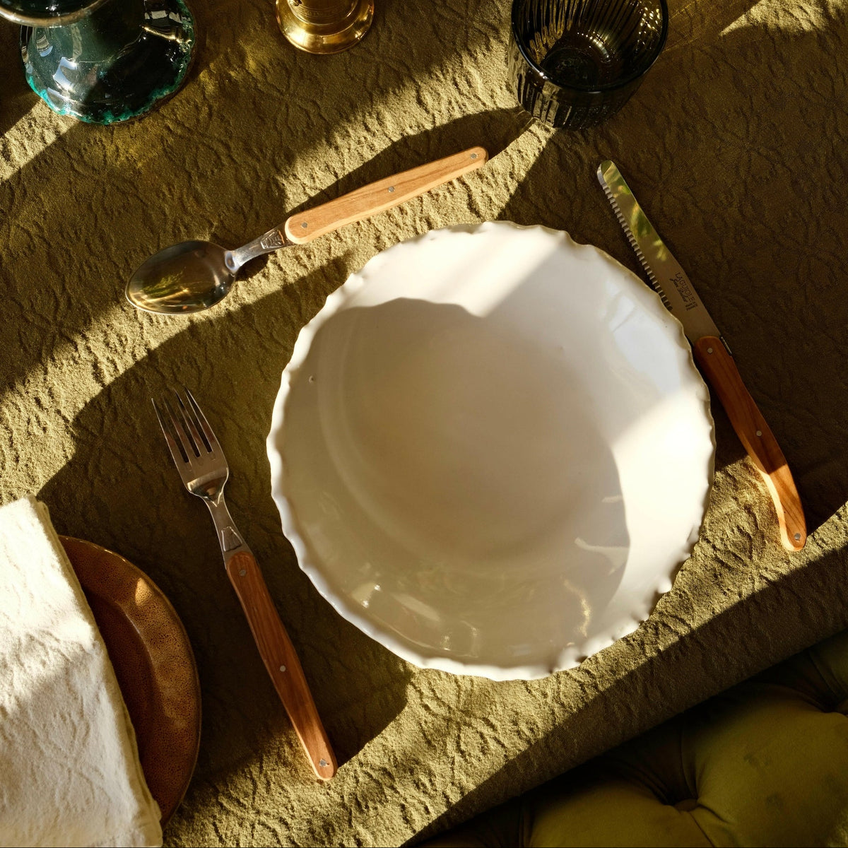 Mantra Living Raw-edged Pasta Bowl in white stoneware, seen from above on an olive linen table with cutlery.