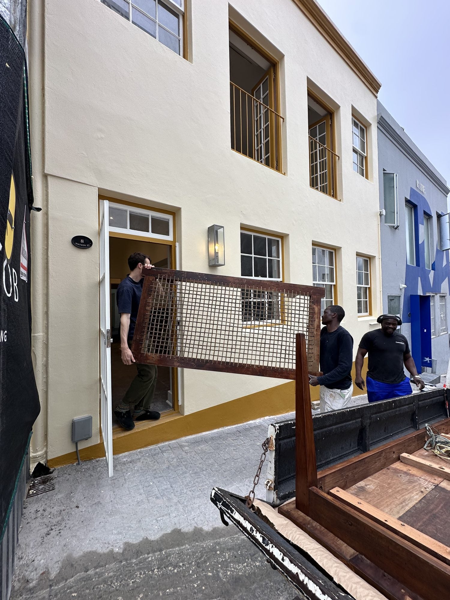 Two people carrying an antique cane and timber screen in through the front door