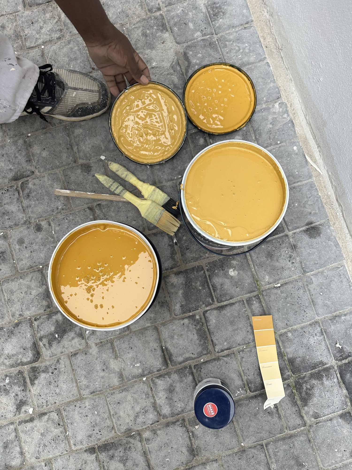 Open tins of ochre paint and brushes on the cobbles