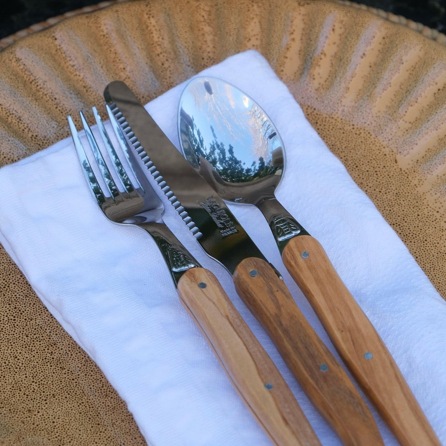 Mantra Living Laguiole olive wood cutlery resting on a pale blue linen napkin on a textured stoneware plate.
