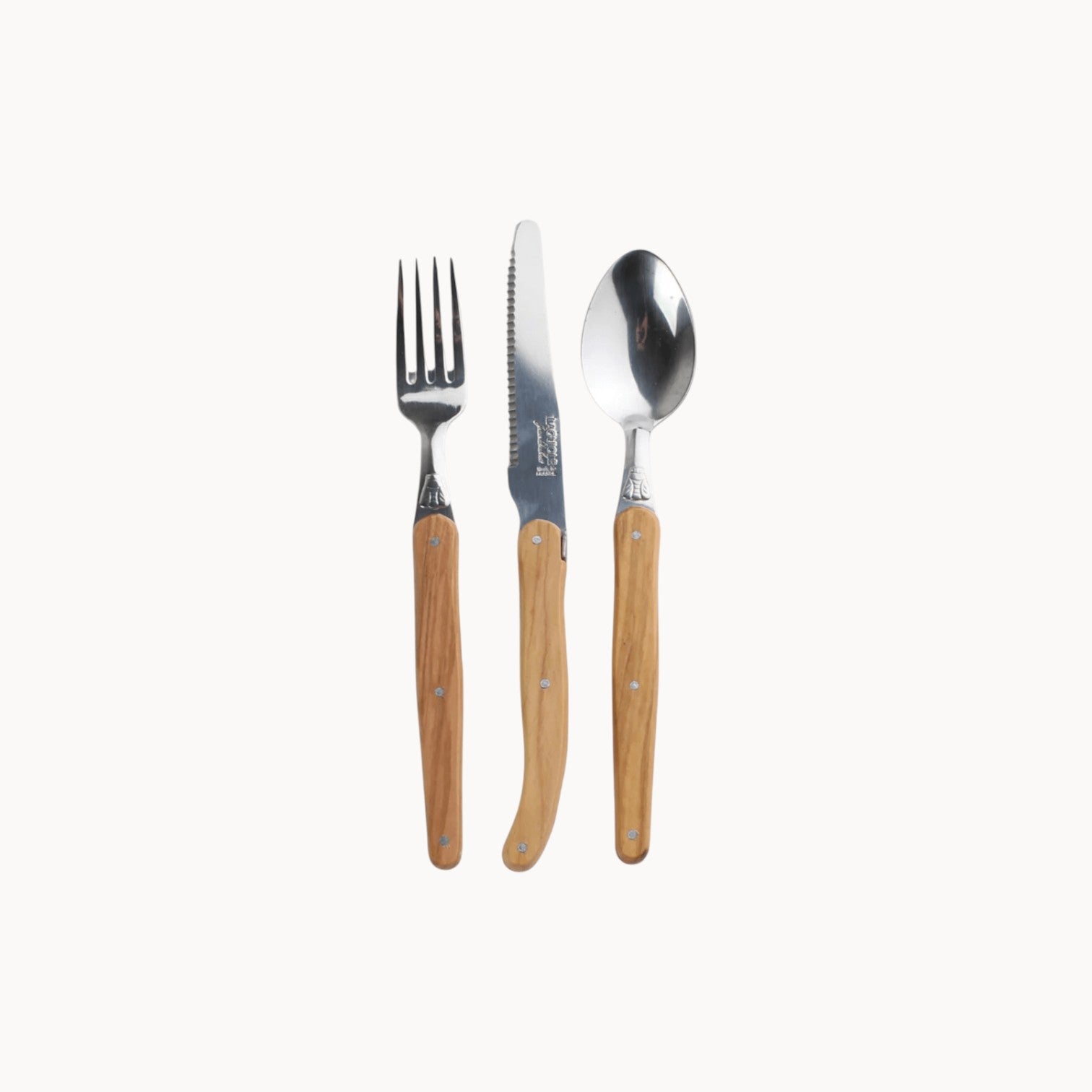 Mantra Living Laguiole cutlery in olive wood and stainless steel, showing the fork, serrated knife and spoon.