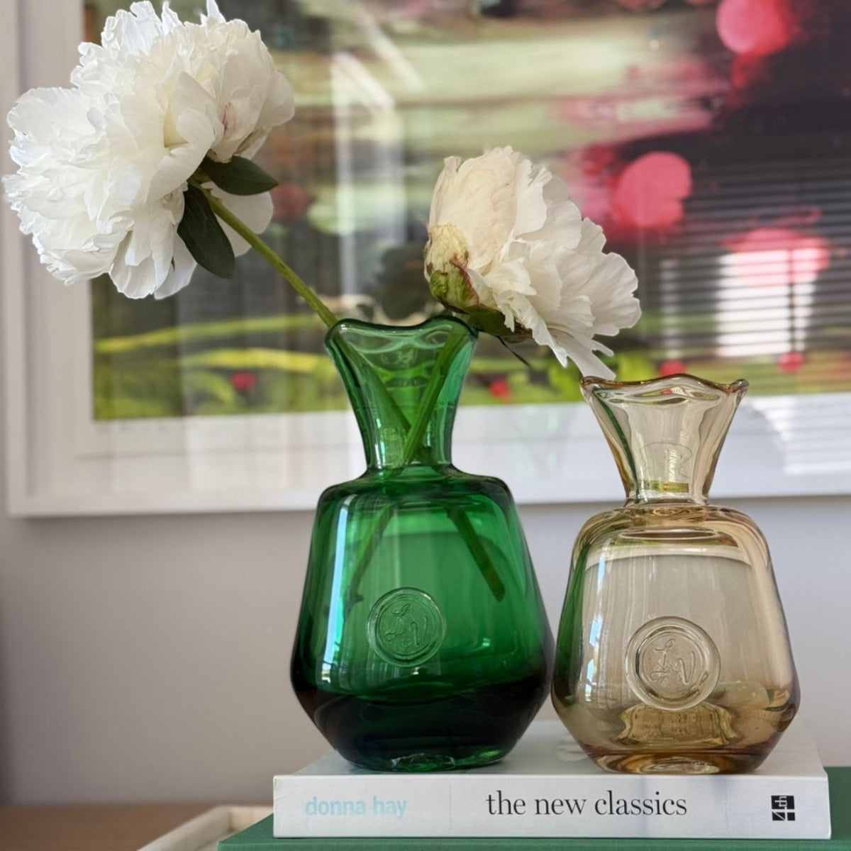 MANTRA LIVING Casa LV Peony Vases in green and amber glass, handcrafted with undulating rims, displayed on stacked books.