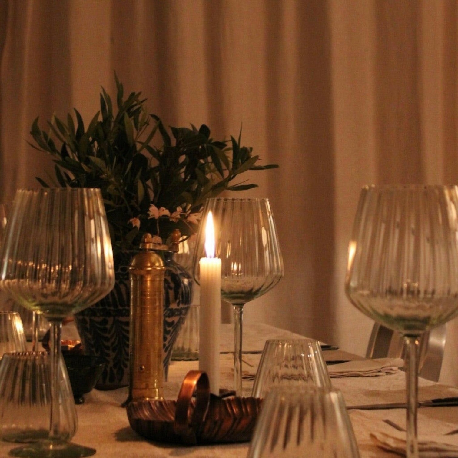 Mantra Living ribbed red wine glasses on a candlelit table with a brass vase of olive branches and amber glass.