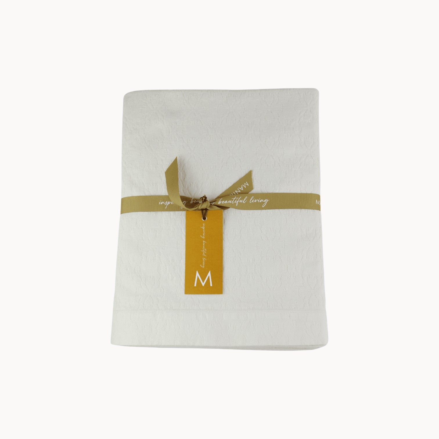 Mantra Living Hibiscus cotton tablecloth in vanilla, folded and tied with an ochre ribbon and gift tag. #Color_Vanilla