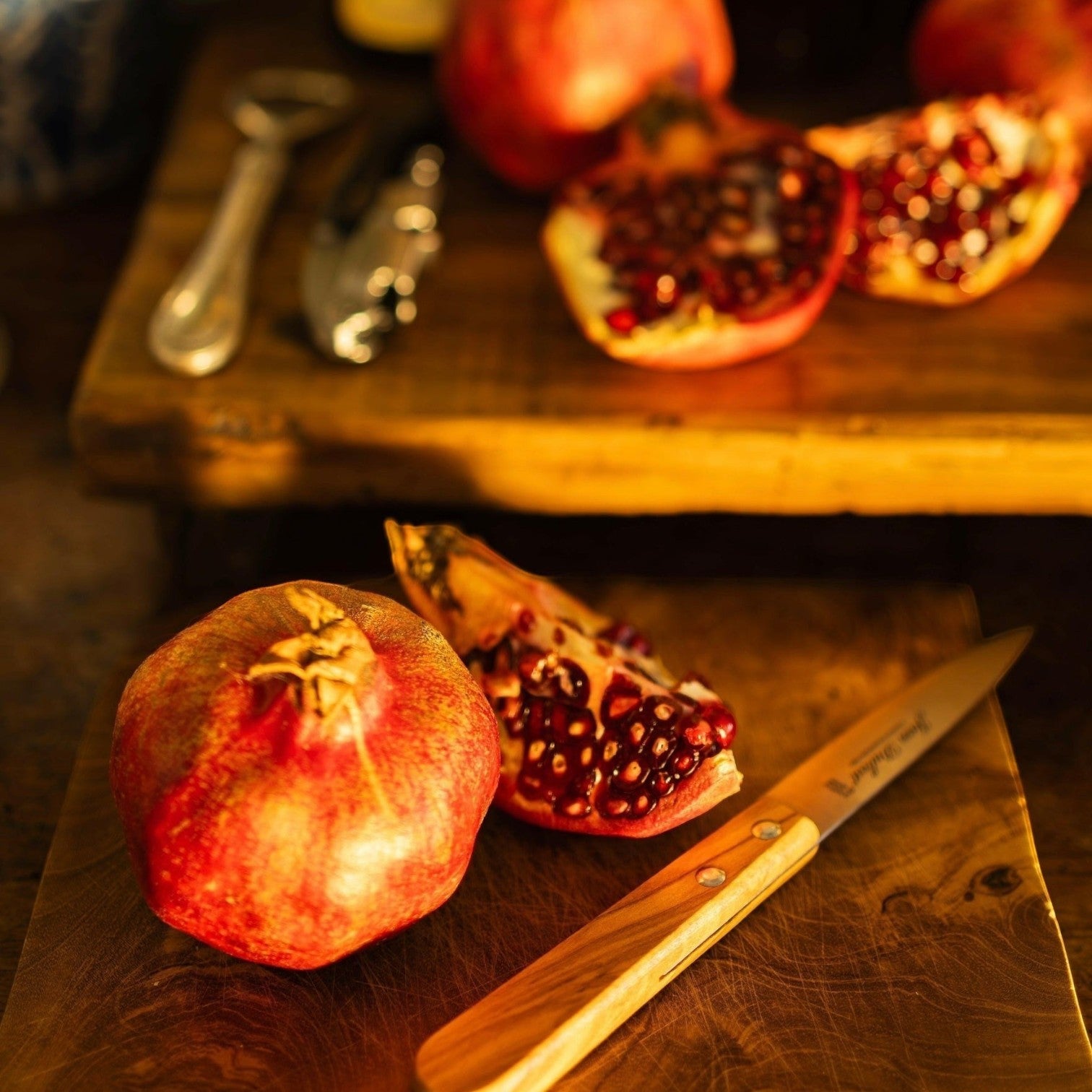 MANTRA LIVING wooden drinks board holding a whole pomegranate, pomegranate slices, and a small paring knife.