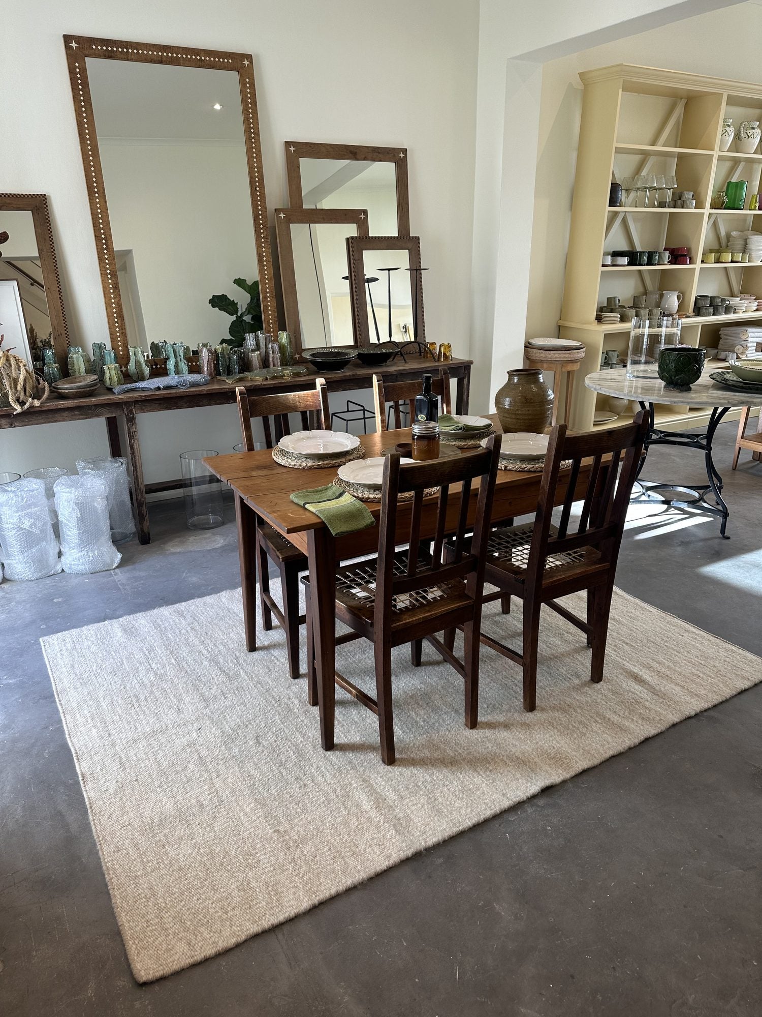 Inside the store: a long timber dining table, chairs, antique mirrors and open shelving